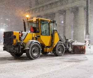 Winter service vehicles. Big yellow snow plow tractor working in city at night in heavy snowfall